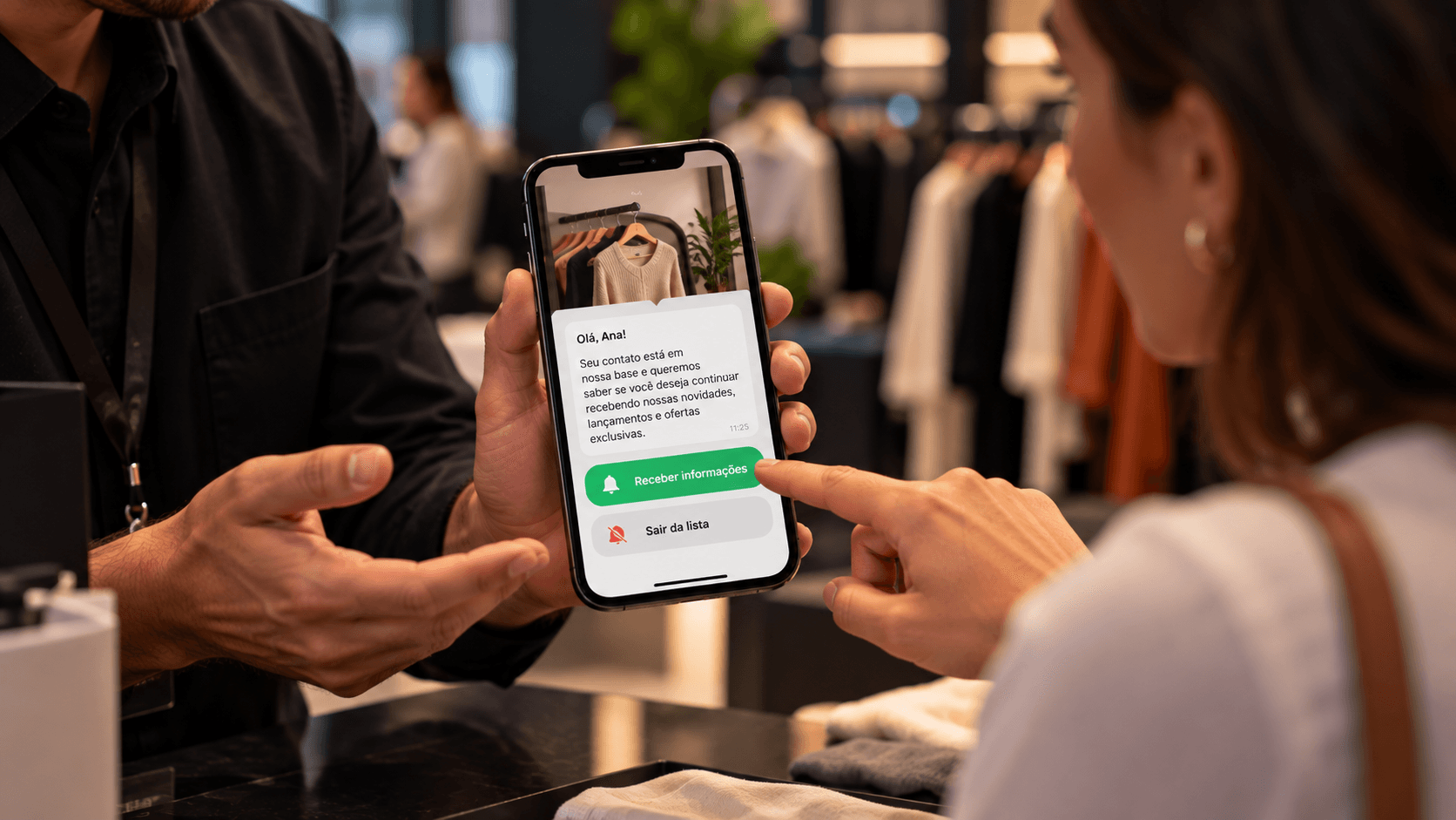 Um vendedor mostra o celular a uma cliente. Na tela, uma mensagem pergunta se ela quer continuar recebendo, com dois botões: “Receber informações”, em verde, e “Sair da lista”.